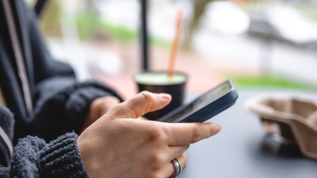Person håller en mobiltelefon, med en kaffekopp bredvid.